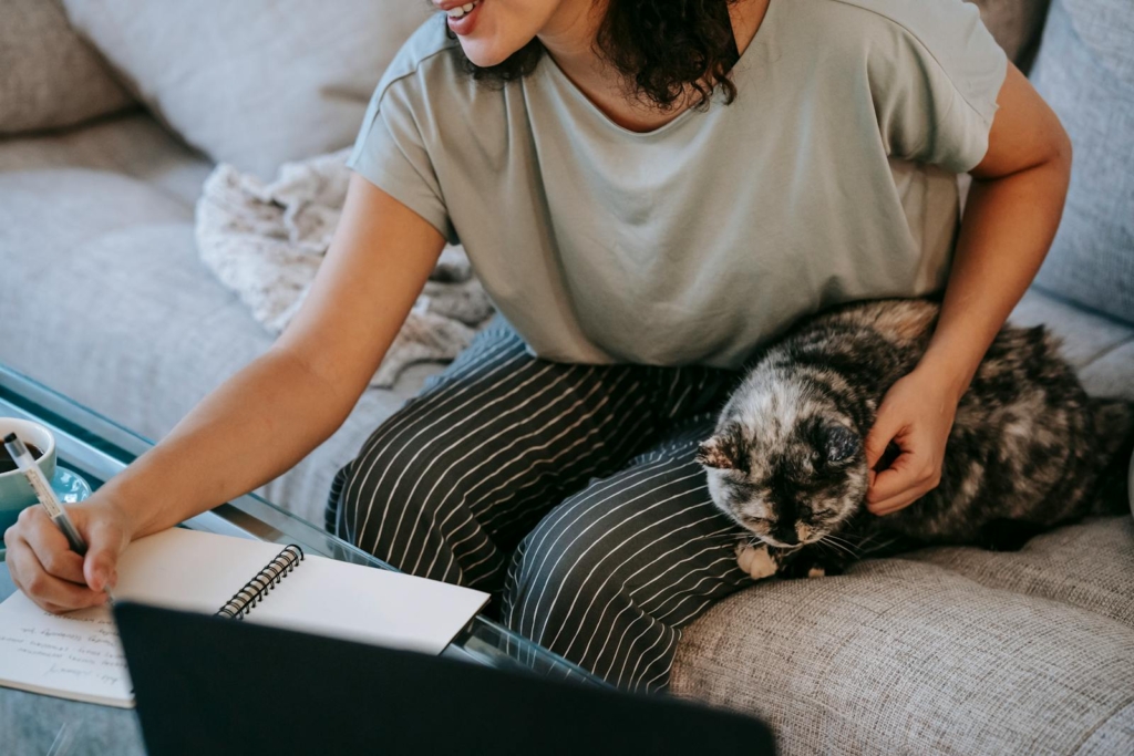 Happy woman stroking cat while writing in planner